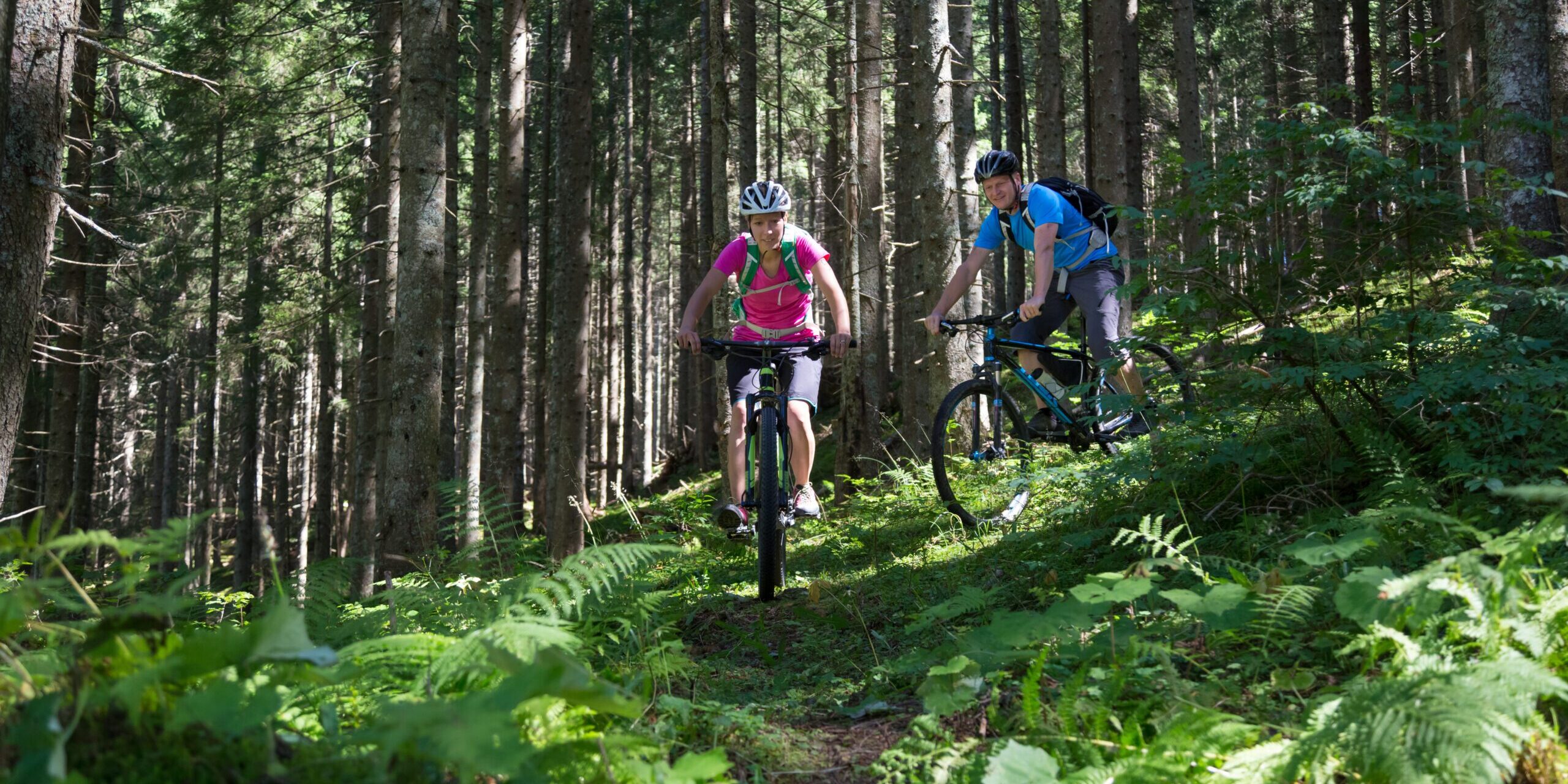 Active sporty couple riding mountain bikes on forest trail .